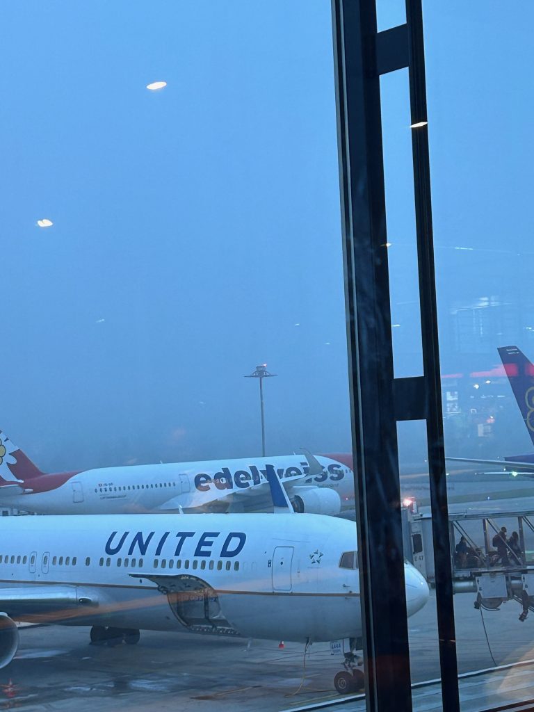 View through an airport terminal window at dusk, with aircraft waiting at the gate.