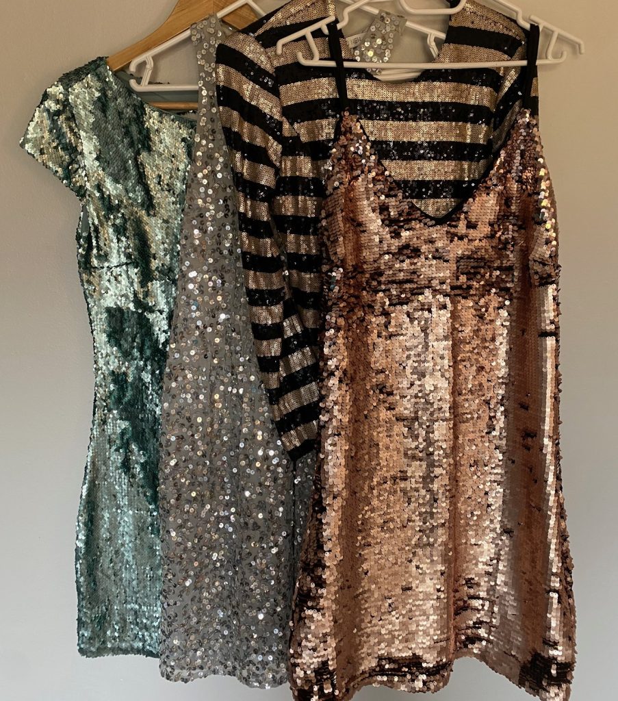 A row of sparkly sequinned party dresses on hangers — the dress-up side of girlhood.